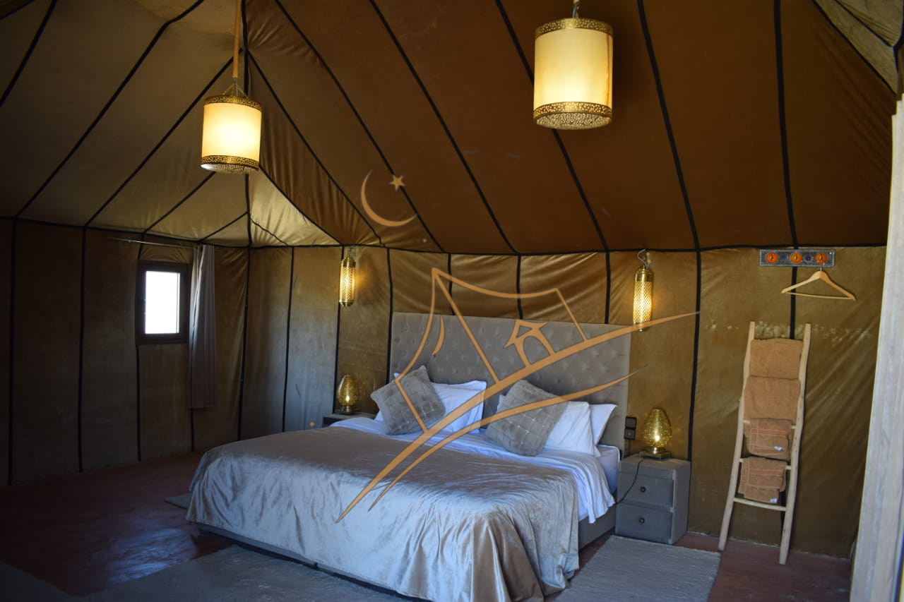 Tufted upholstered bed beneath brass pendant lanterns in a luxury desert tent