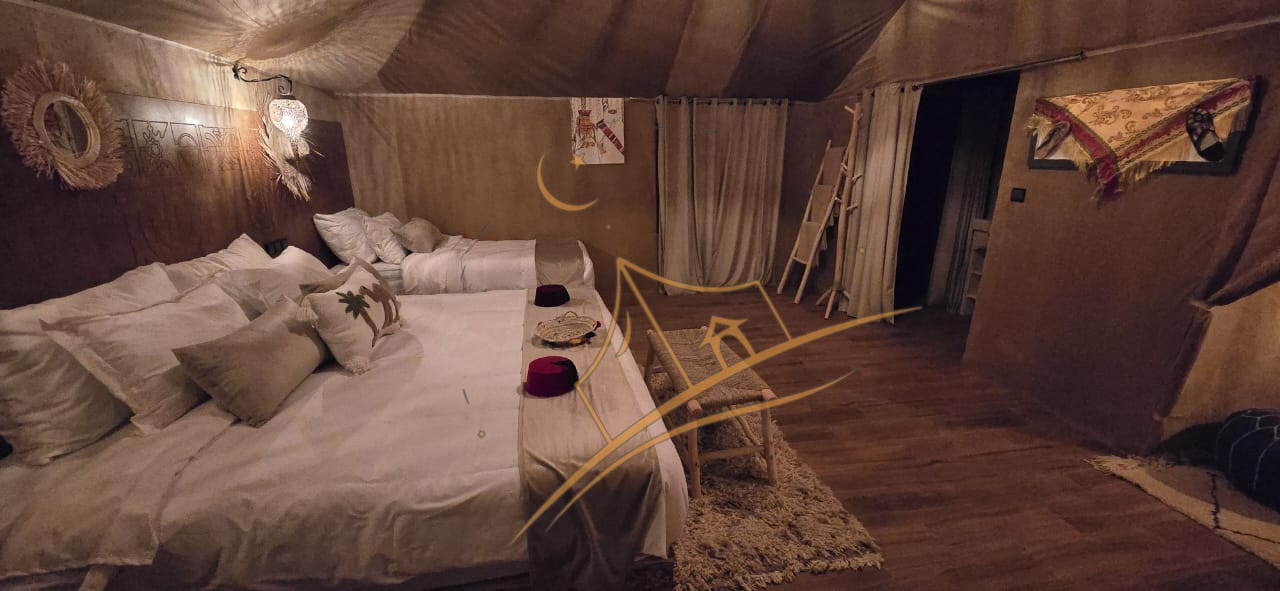 Twin beds dressed in warm linens beneath a sunburst mirror in a softly lit tent bedroom