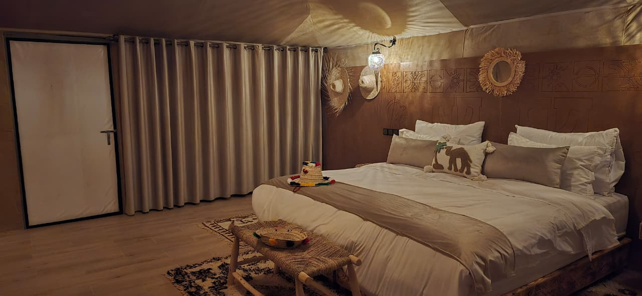 Tent bedroom with hand-carved Berber wall motifs, a sunburst mirror and an embroidered camel cushion