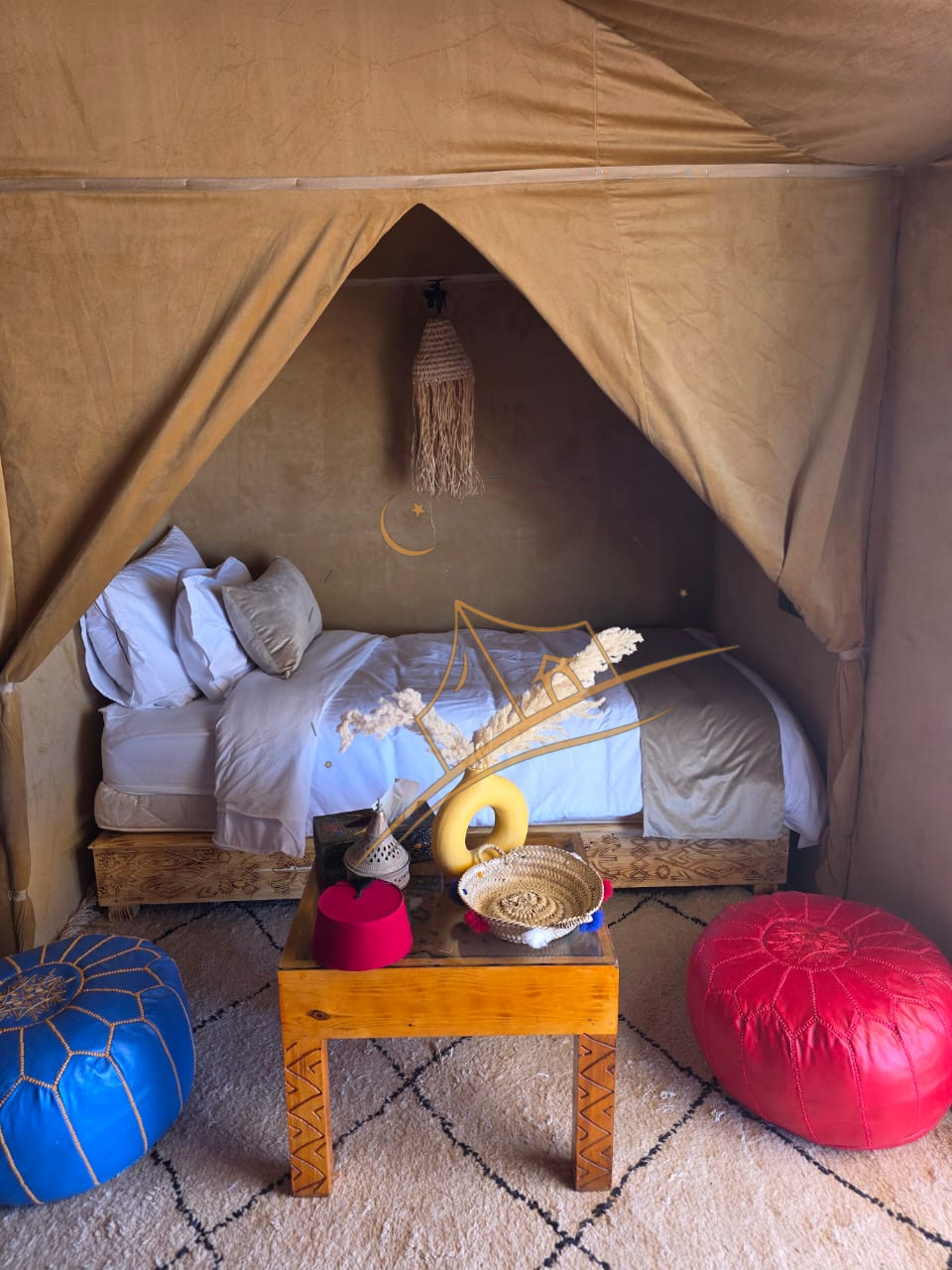 Canopied bed nook framed by the tent's peak, flanked by blue and red leather poufs