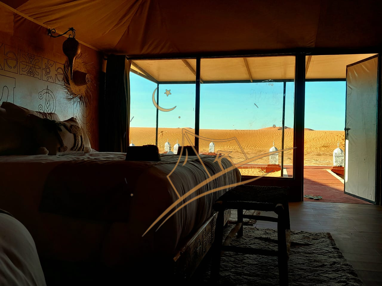 Silhouetted tent bedroom opening onto a floor-to-ceiling view of the golden dunes at sunrise