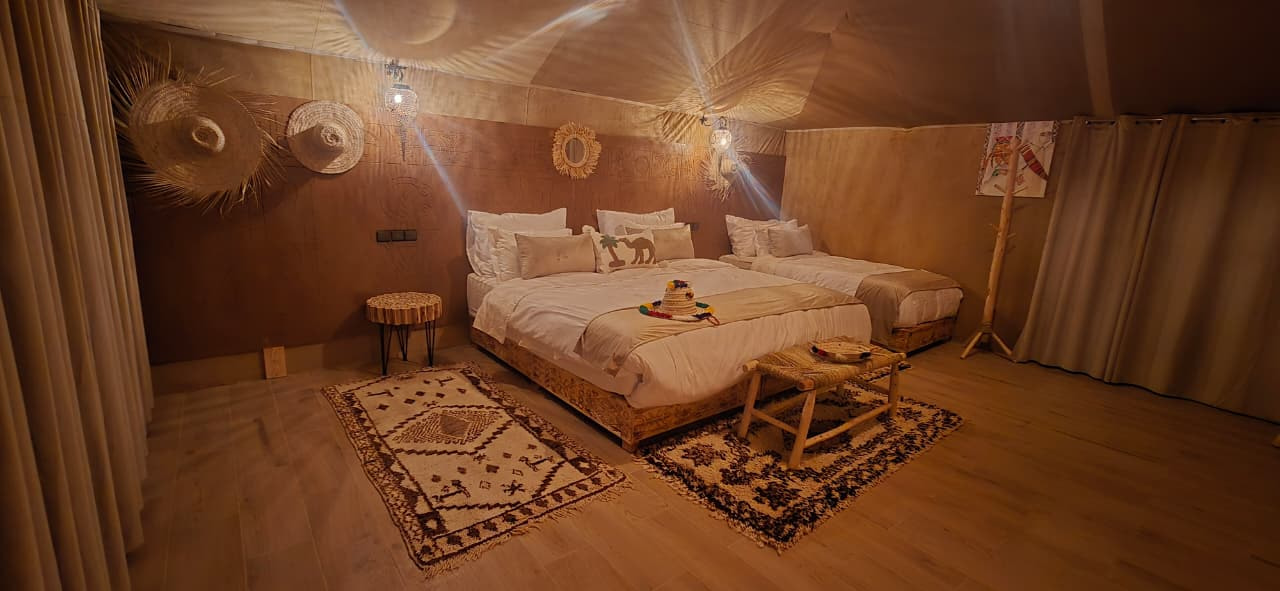Twin-bed tent interior with layered Beni Ourain rugs and woven straw hats hung above the headboard