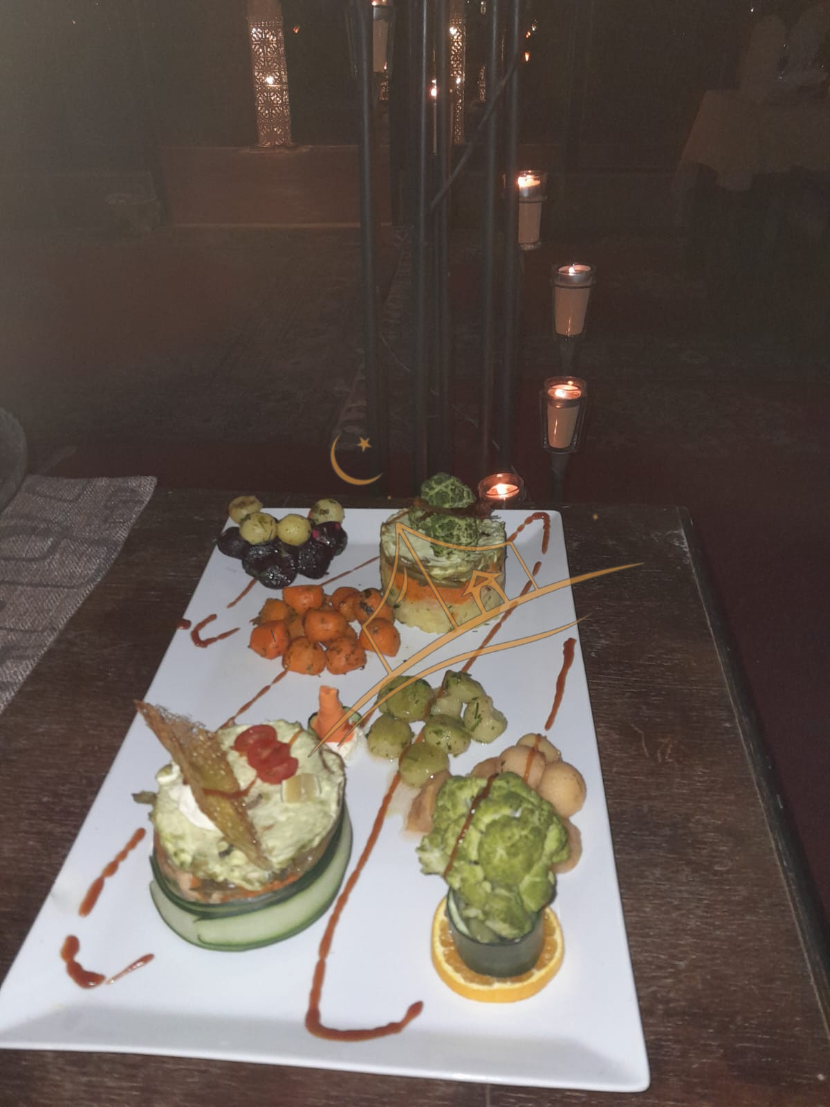 Plated vegetable appetizers with sauce-drizzle art beside a glowing candelabra