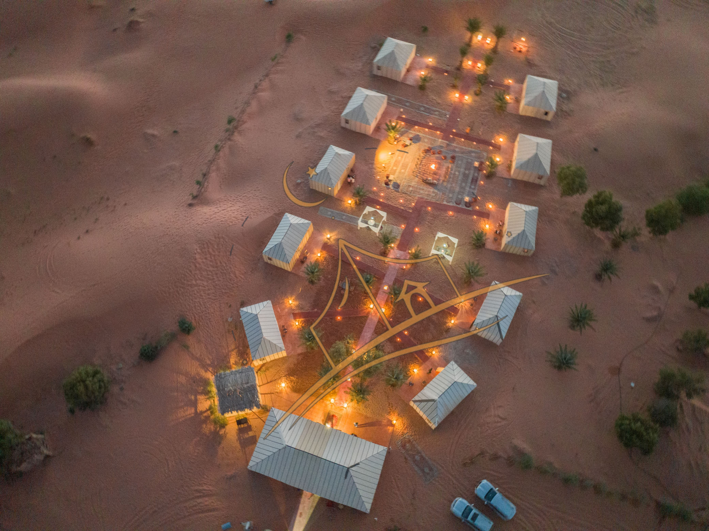 Aerial dusk view of Sahara Night Camp's lantern-lit tents nestled among the Erg Chebbi dunes