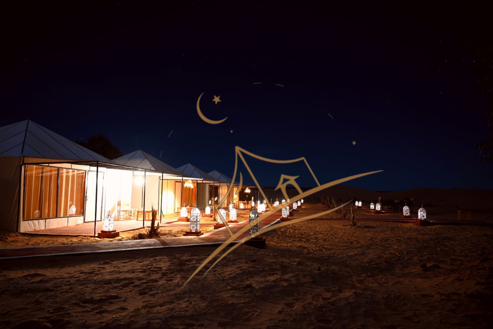 Row of illuminated luxury tents beside open dunes at blue hour