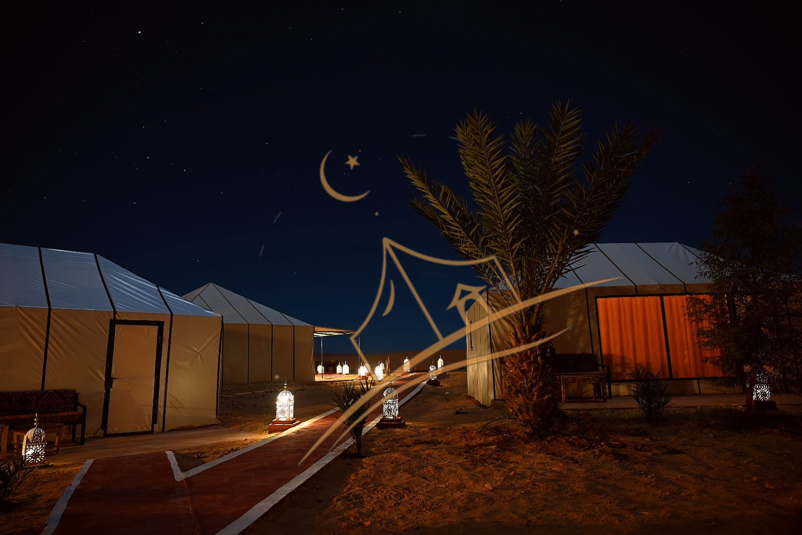 Lantern-lined pathway between luxury tents glowing under a deep blue desert sky