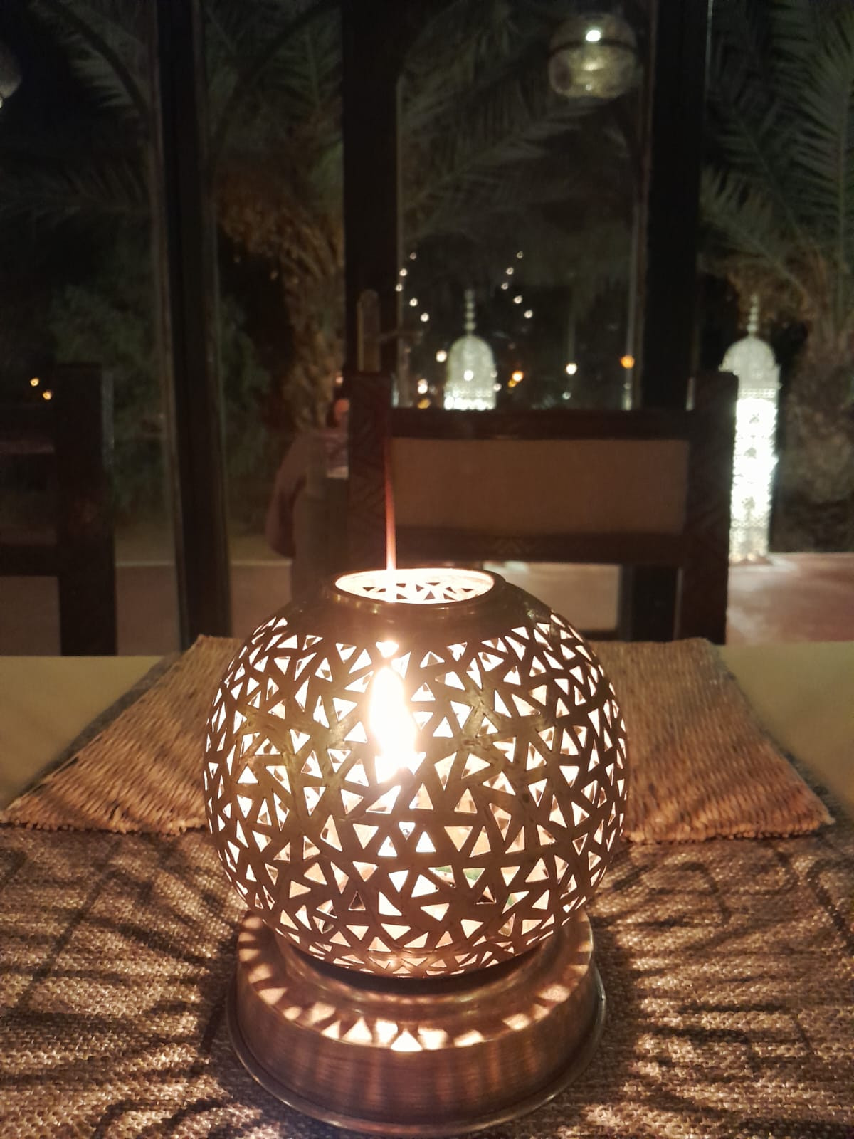 Close-up of a hand-cut brass Moroccan lantern glowing with candlelight on a dining table
