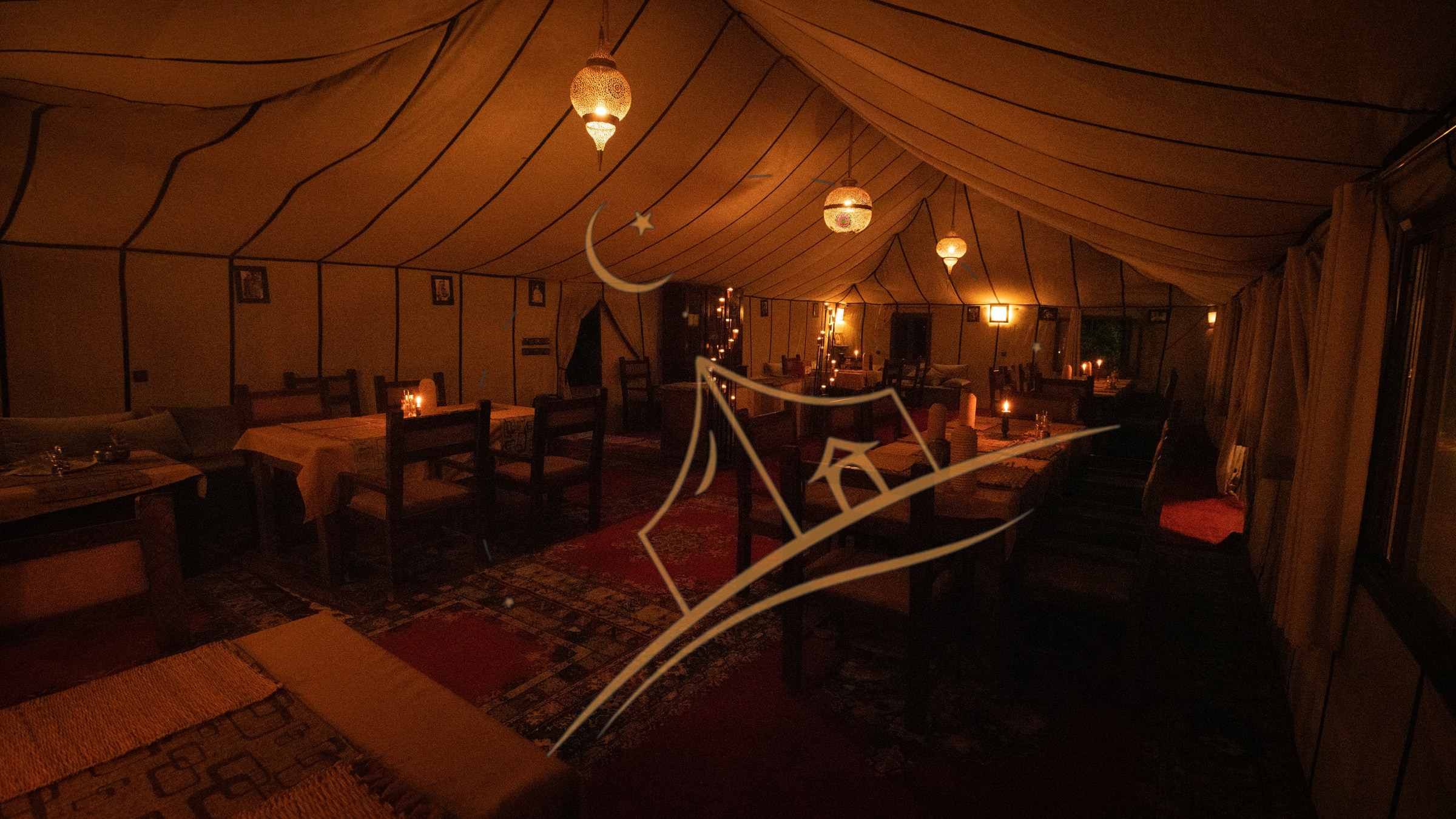 Empty candlelit dining tent glowing with hanging Moroccan pendant lanterns