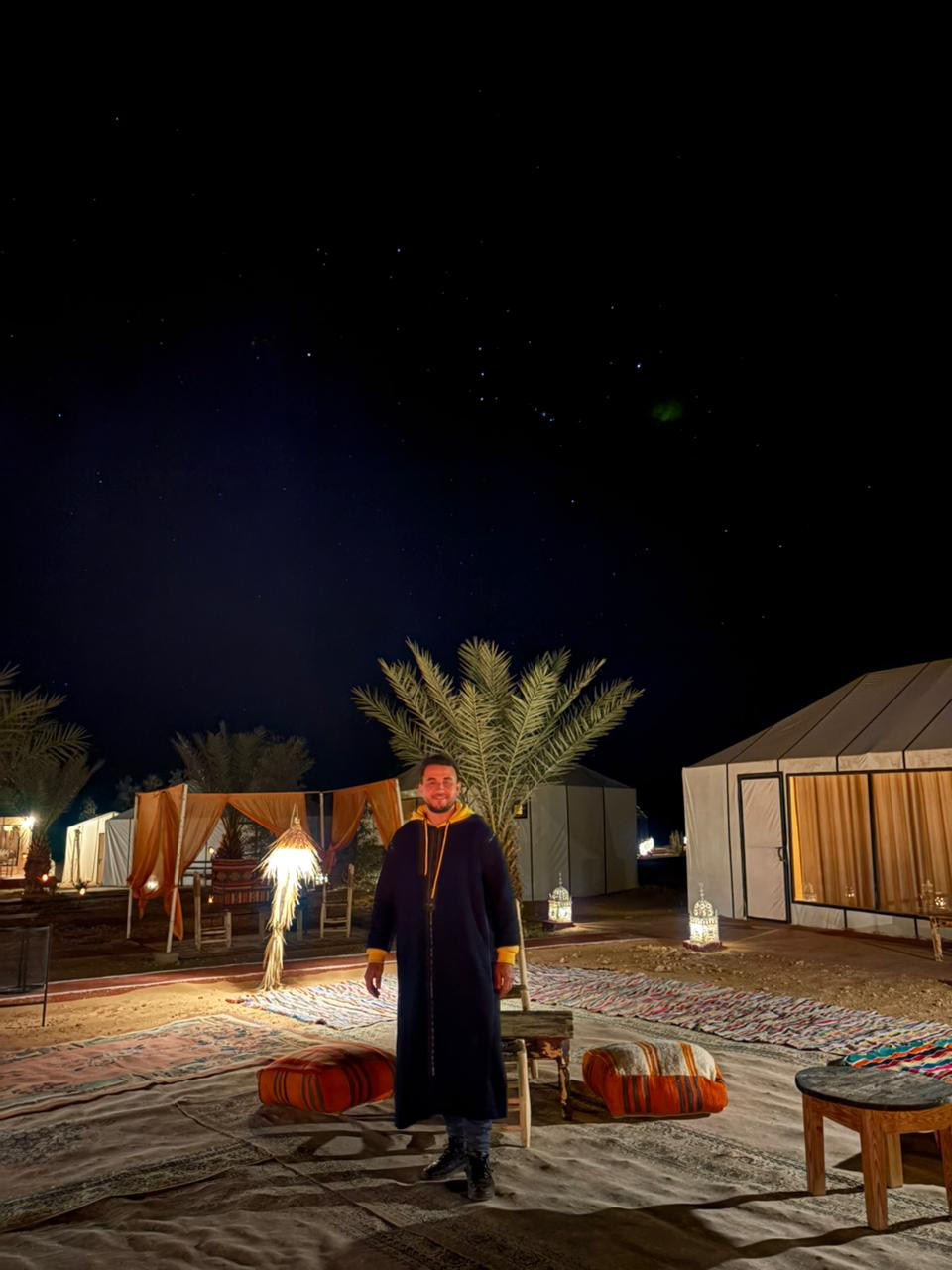 Said Oujil, owner of Sahara Night Camp, standing among lantern-lit tents beneath a starry desert sky